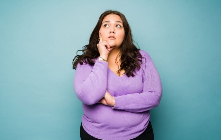 Mujer con jersey morado en actitud pensativa sobre un fondo azul