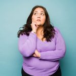 Mujer con jersey morado en actitud pensativa sobre un fondo azul